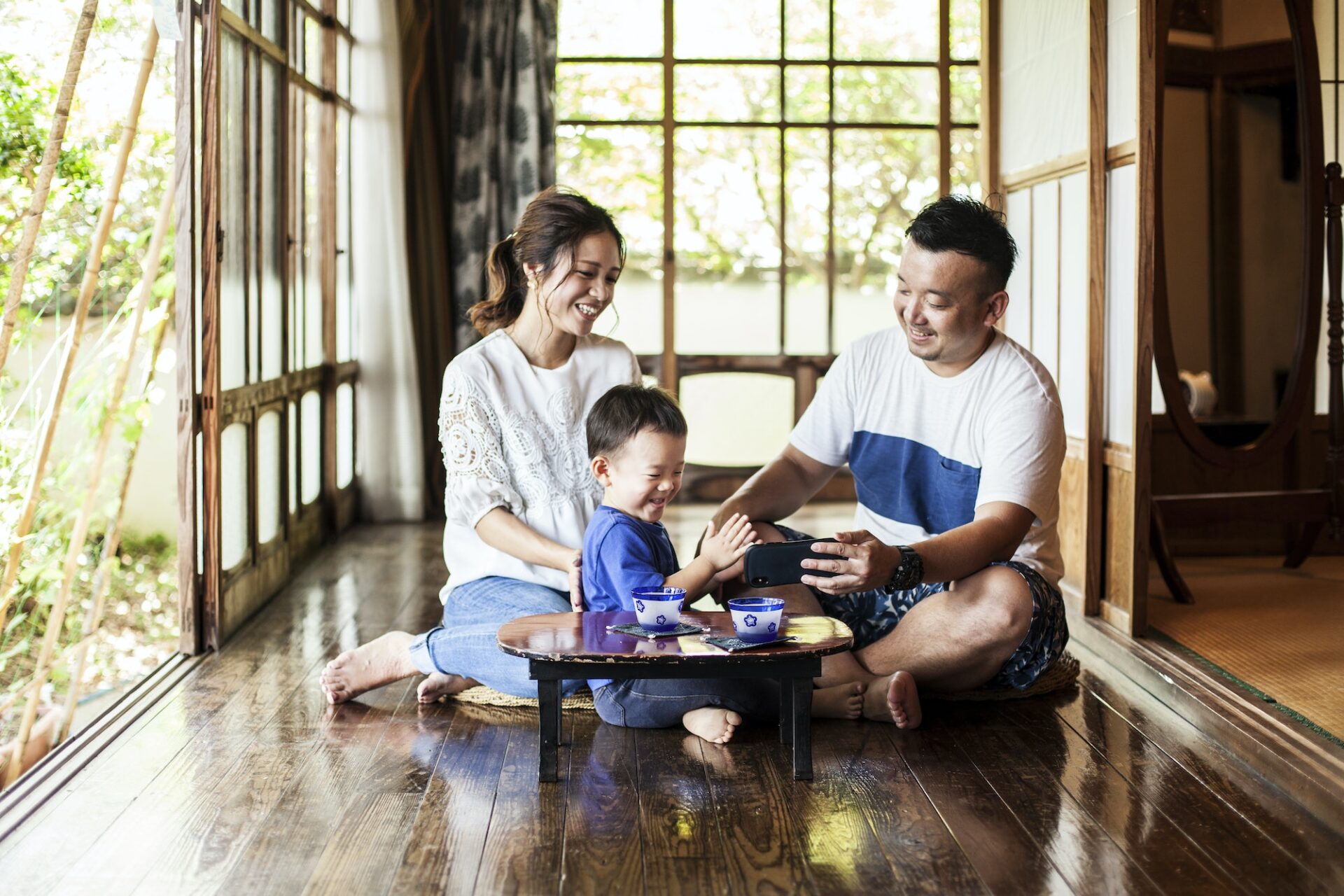 Japanese woman, man and little boy on a porch drinking tea.
